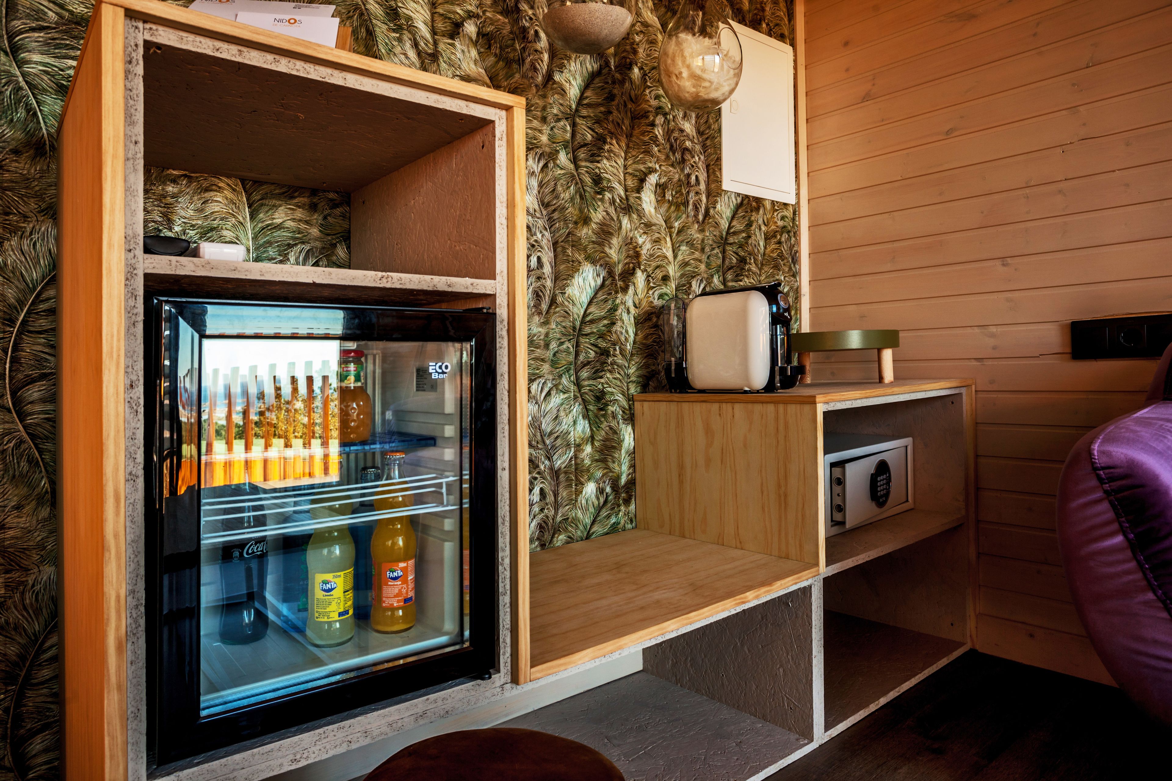 A compact room with a refrigerator stocked with beverages, a coffee maker, and a small cabinet.