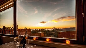 A table with a bottle of champagne, two glasses, and three candles by a window with a sunset view. - Nidos de Carnota (Carnota)