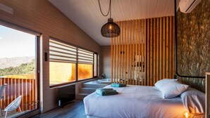 A modern bedroom with a large bed, a bedside table with a lamp, a window with blinds, and a view of the outdoors. - Nidos de Carnota (Carnota)