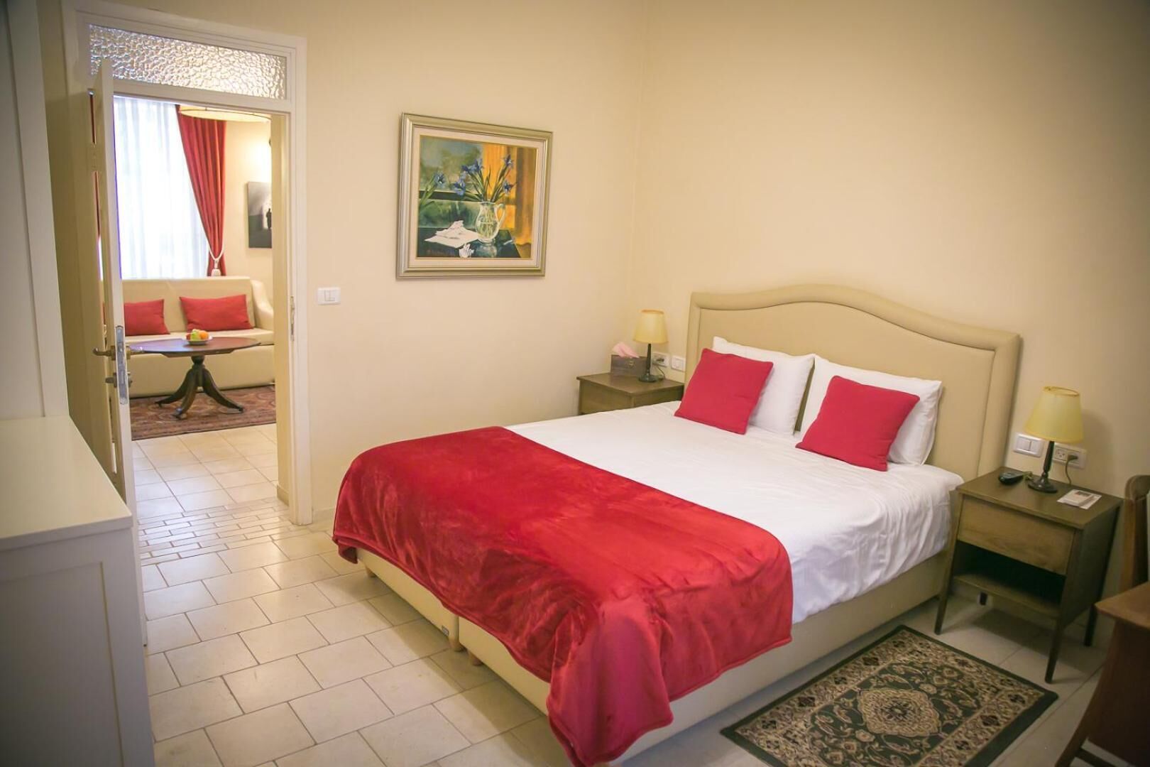 Habitación de hotel con una cama grande, dos mesitas de noche, un atril y una vista de la habitación contigua.
