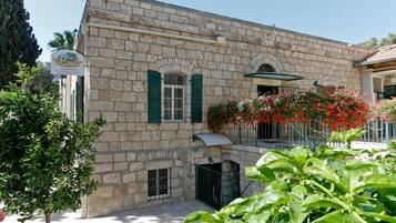Un edificio de piedra con contraventanas verdes, un balcón adornado con flores rojas y una puerta pequeña.
