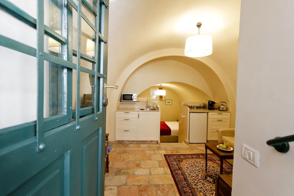A compact kitchen with a microwave, sink, and small refrigerator. A dining area with a table and chairs is visible, along with a patterned rug on the floor.
