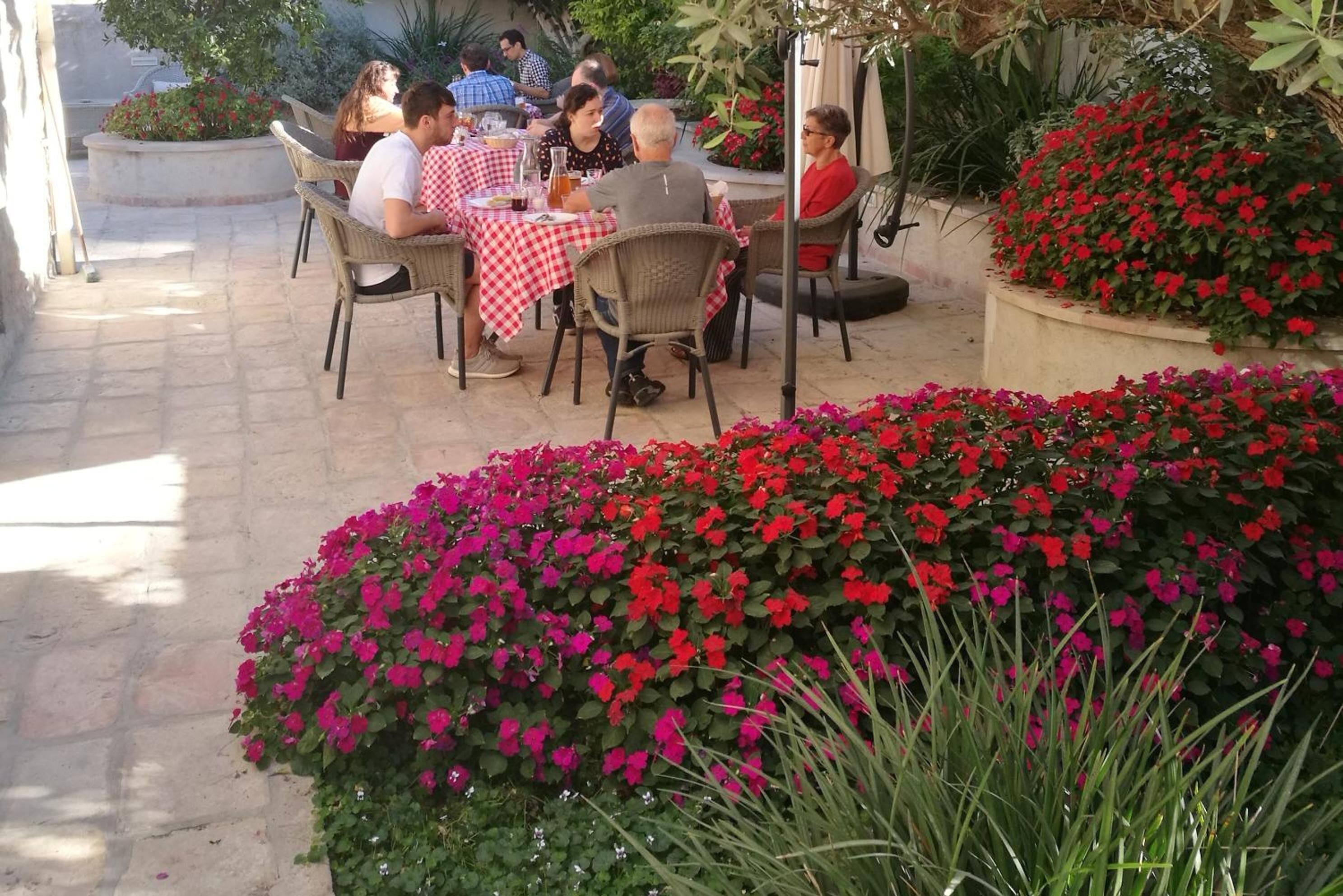 Un patio al aire libre con sillas y mesas de mimbre, rodeado de flores rojas y rosas vibrantes.