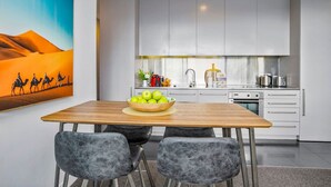 A modern kitchen with white cabinets, a wooden dining table, and two chairs. - Sunlit City Fringe Apartment wth Heat Pump+Carpark (Auckland)