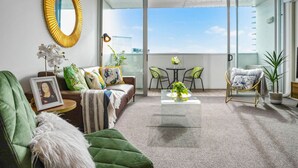 A modern living room with a sofa, a green armchair, a coffee table, and a balcony with a view. - Sunlit City Fringe Apartment wth Heat Pump+Carpark (Auckland)