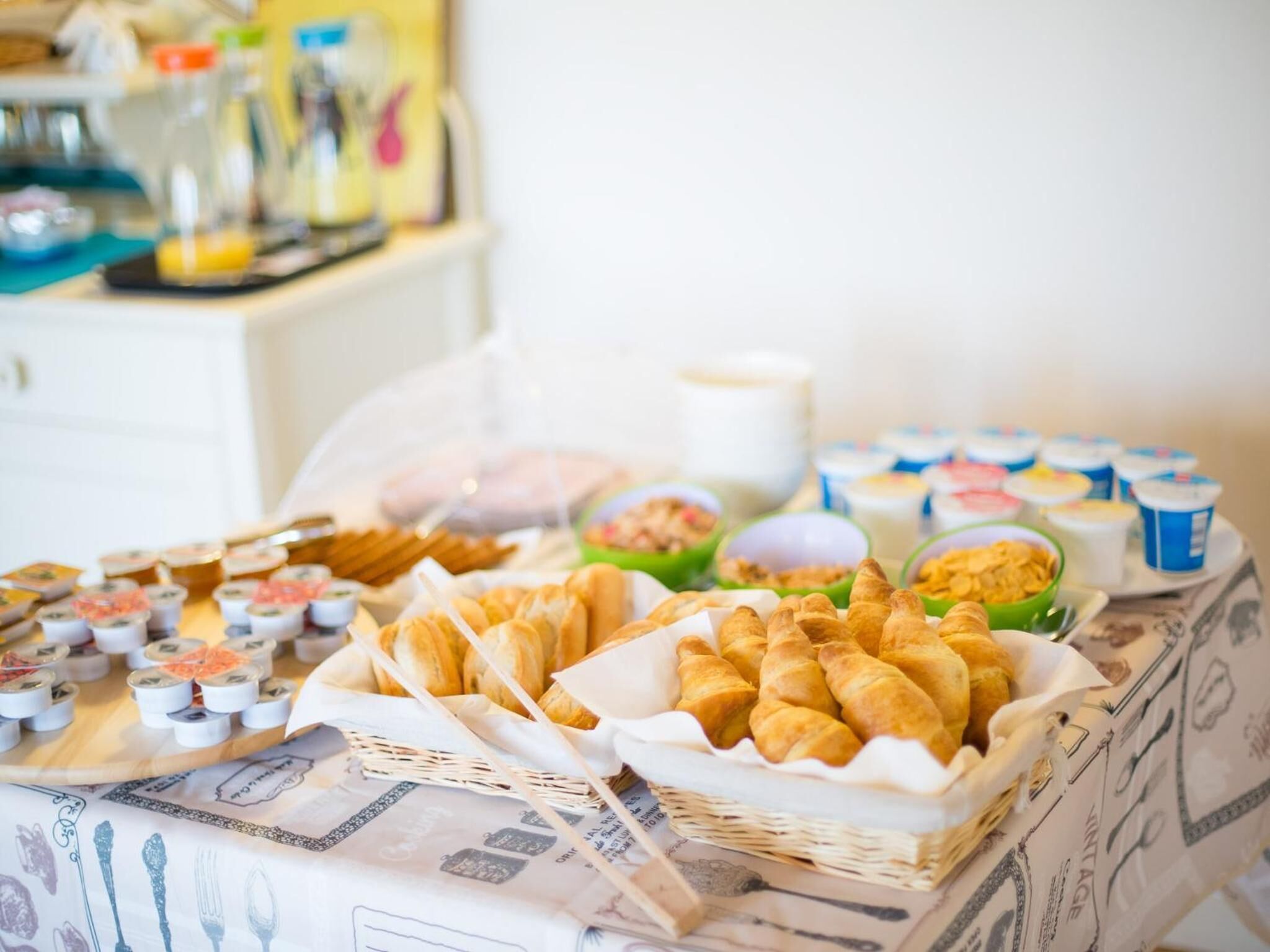 Une table de buffet proposant divers plats et aliments, présentés dans différents récipients, notamment des croissants et de petits bols remplis de nourriture.