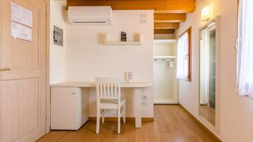 Una habitación compacta con techo de madera, un escritorio pequeño blanco con una silla, un armario blanco y un equipo de aire acondicionado blanco.