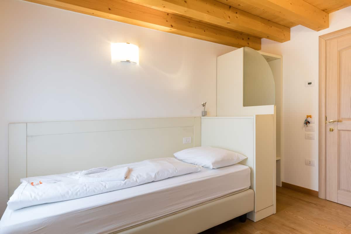 Een enkel bed met wit beddengoed, een houten plafond en een wandlamp.