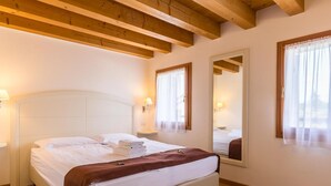 Ein Hotelzimmer mit einem Bett, Holzbalkendecke, einem großen Spiegel und einem Fenster mit Vorhängen.