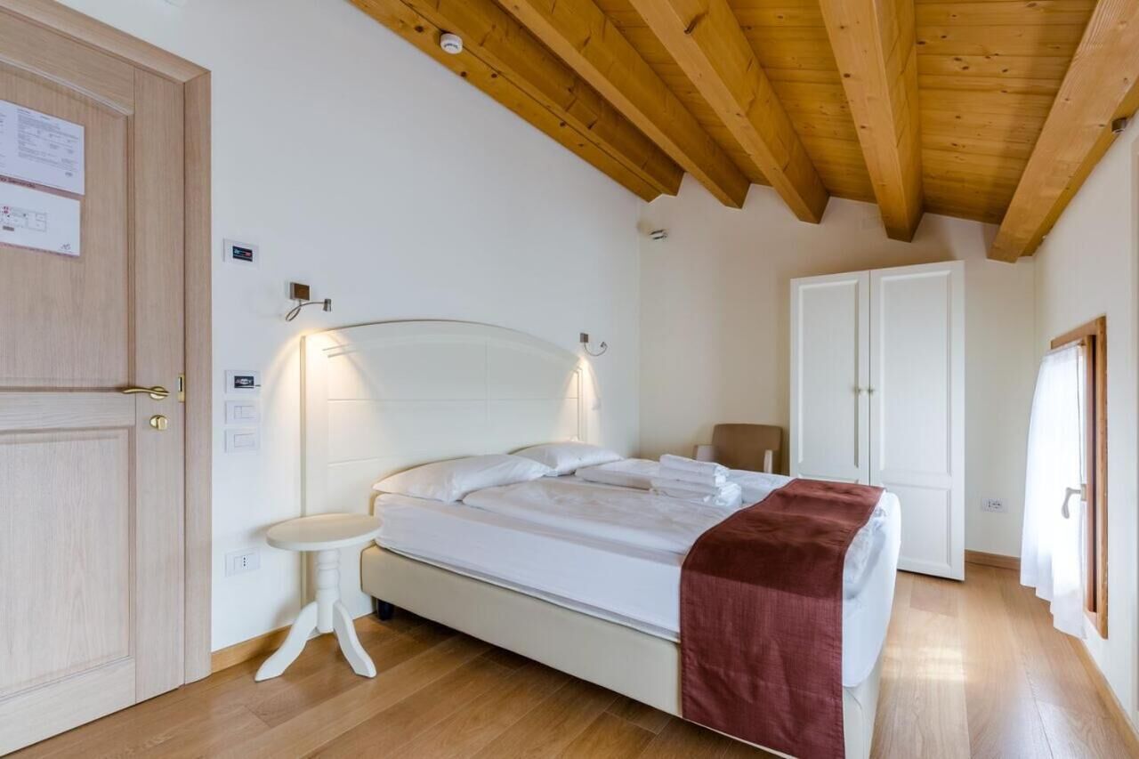Een slaapkamer met een houten plafond, een bed met wit beddengoed, een nachtkastje en een deur.