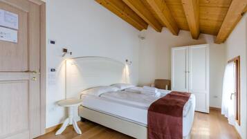 Een slaapkamer met een houten plafond, een bed met wit beddengoed, een nachtkastje en een deur.