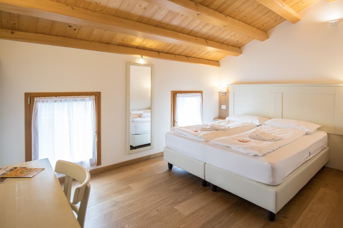 Een slaapkamer met een houten plafond, een groot bed, een nachtkastje en een stoel.
