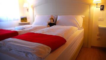 A hotel room with two beds, white bedding, a red blanket on one bed, and a nightstand with a lamp.