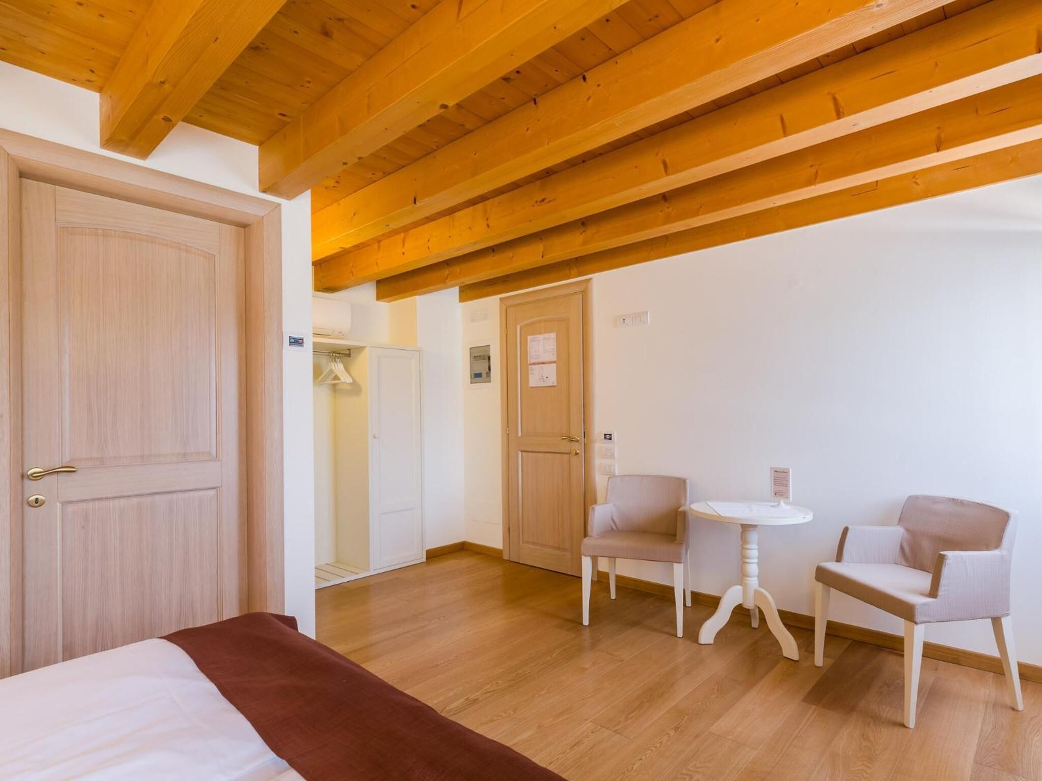 A room with wooden beams, a bed, two chairs, a small table, and a wardrobe.