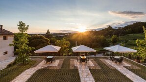 Eine Außenpatio mit Tischen und Sonnenschirmen, mit Blick auf eine malerische Landschaft bei Sonnenuntergang.