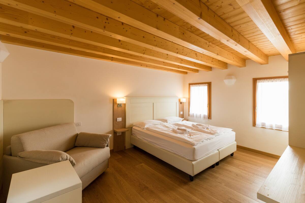 Een slaapkamer met een houten plafond, een bed, een nachtkastje en een bank.