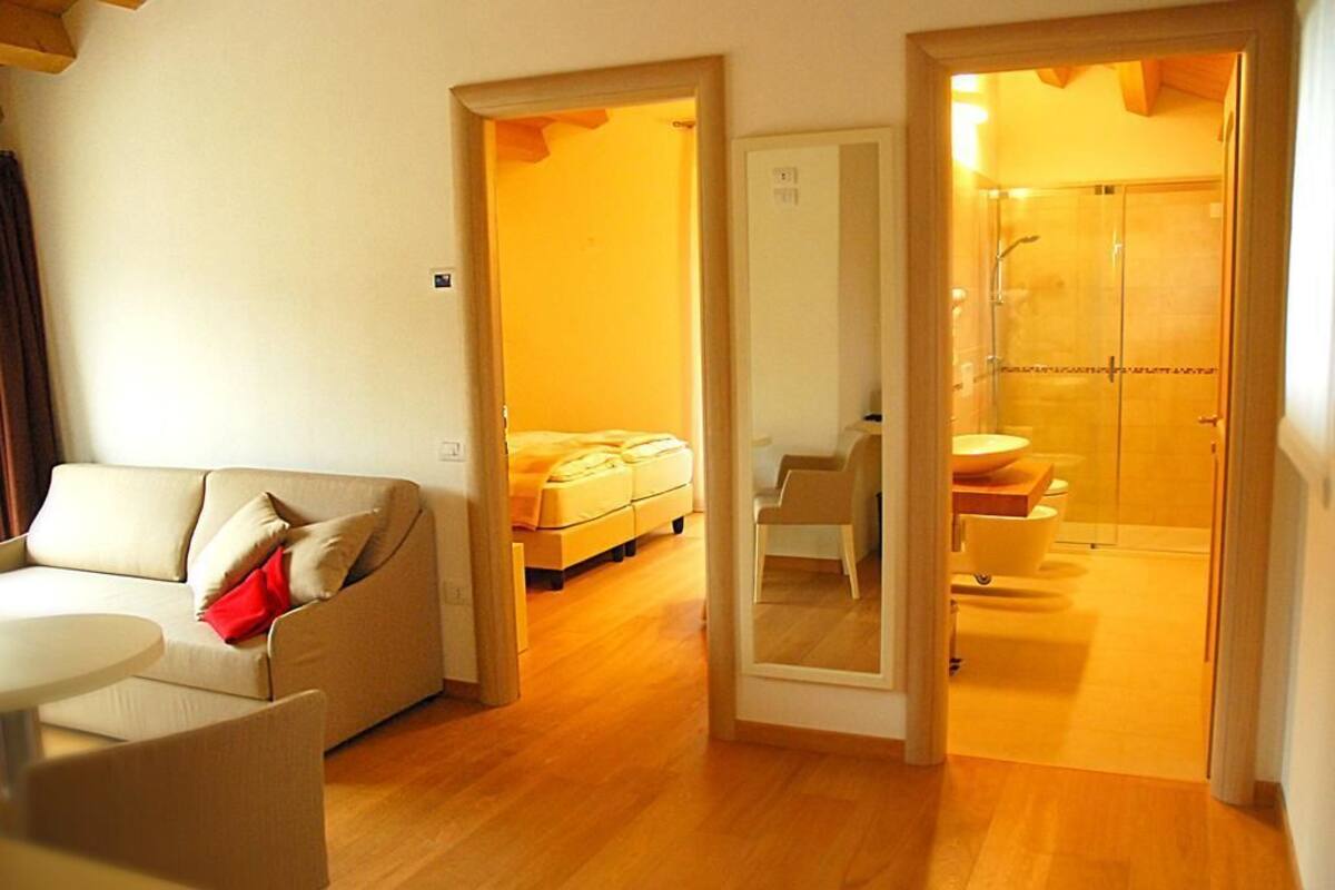 Hotelkamer met houten vloer, een bank, bed, een kleine tafel en een badkamer met een douchecabine van glas.