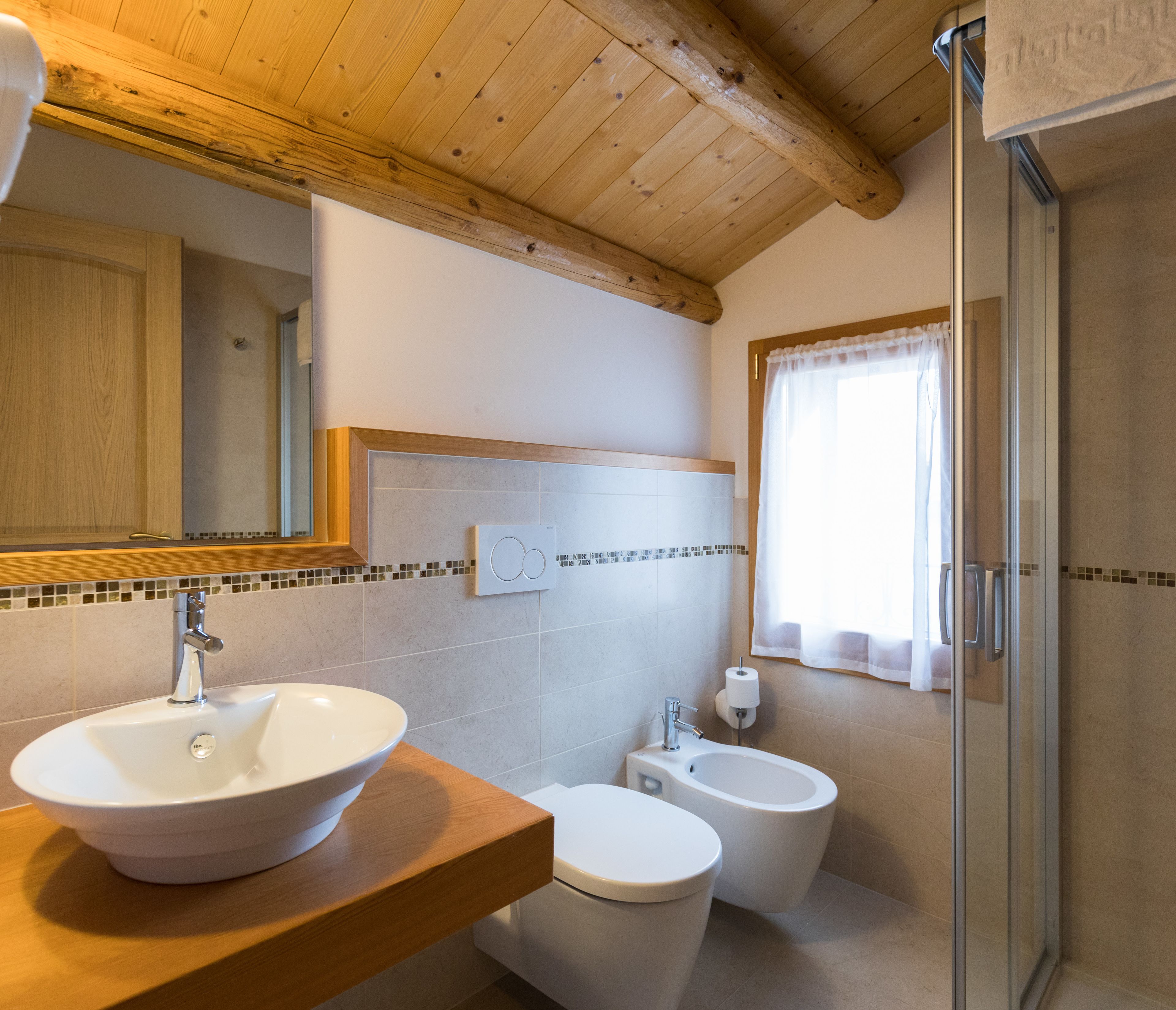 A bathroom with a wooden ceiling, a large mirror, a sink, a bidet, and a shower.