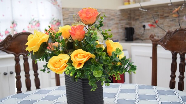 A black vase with yellow and orange flowers on a table with a blue and white patterned tablecloth. - Justinn Apartments (Gros Islet)