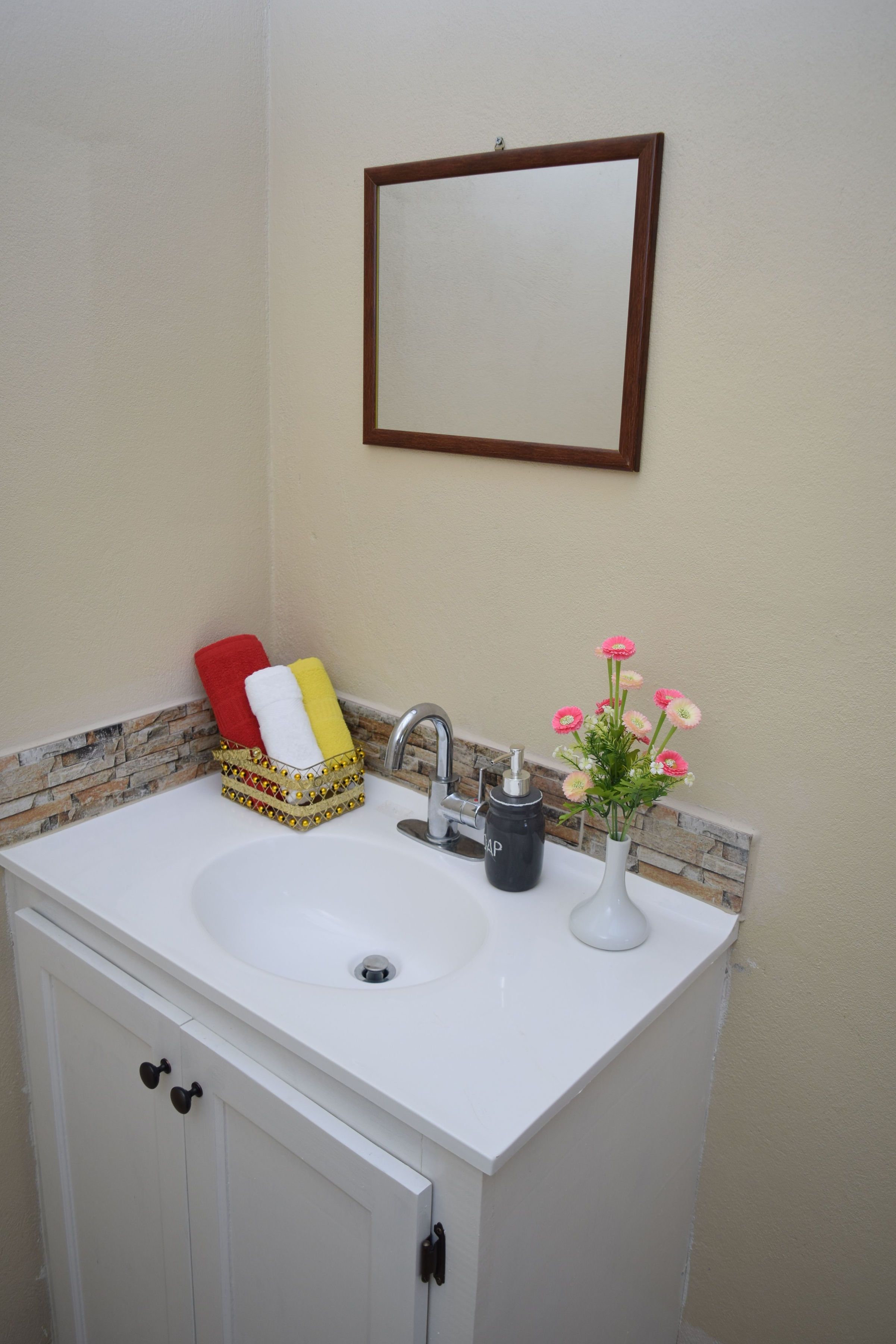 Une salle de bain avec un lavabo blanc, un miroir, un vase de fleurs et un panier rempli de serviettes.