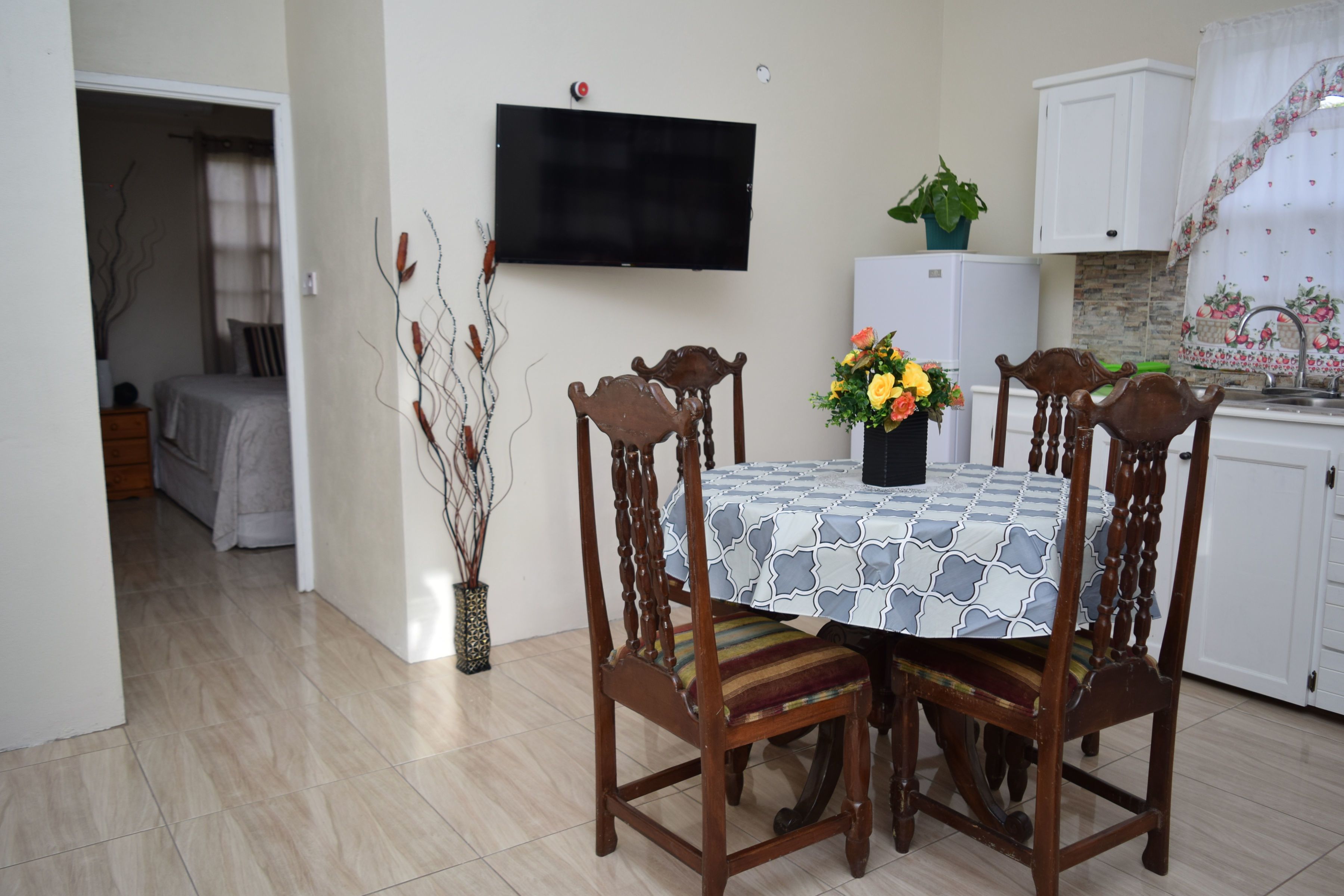 A dining area with a table, chairs, a TV, and a kitchen in the background.