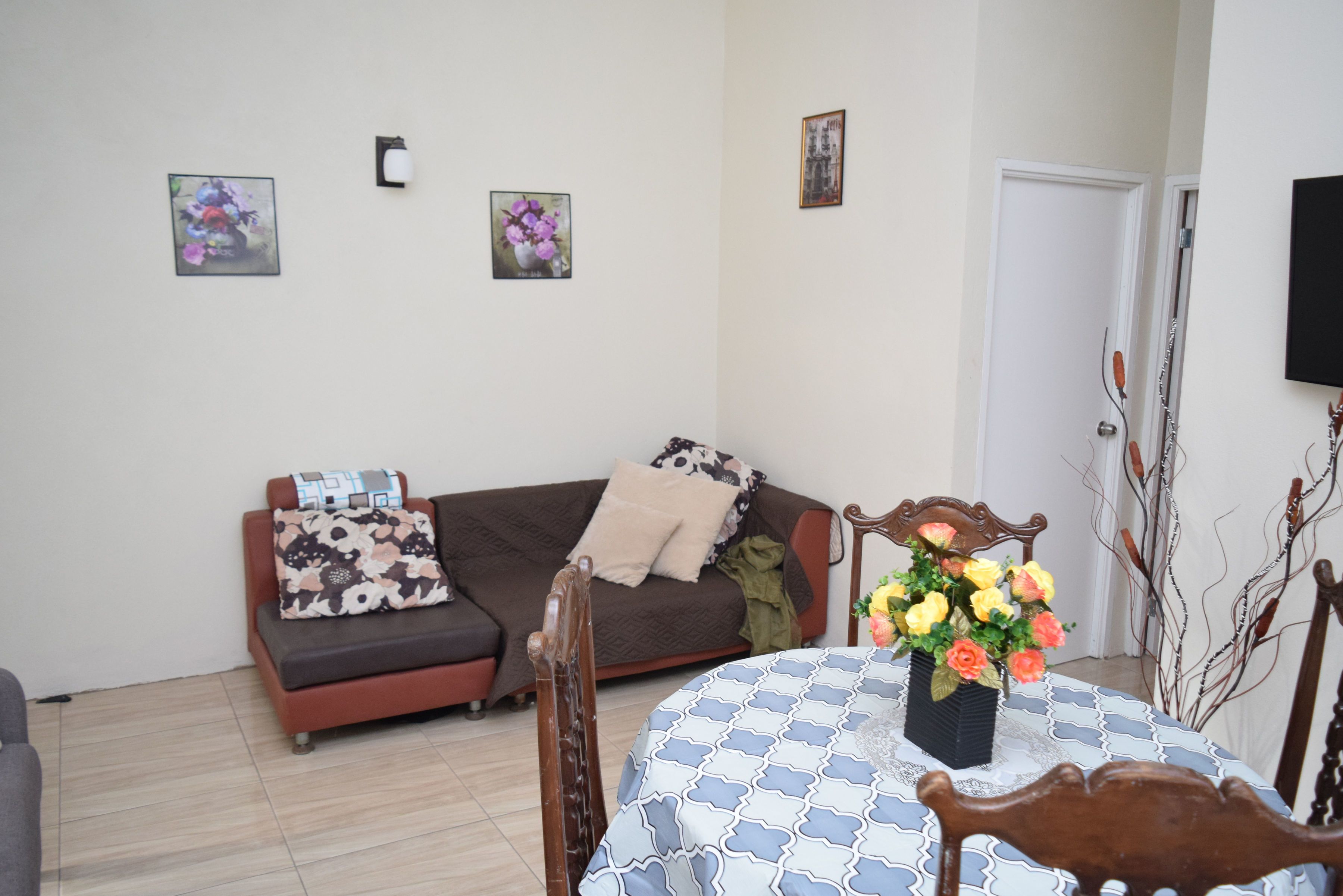 A living room with a sofa, a dining table with a vase of flowers, and a chair.