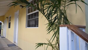 A corridor with a yellow wall, white doors, and a wooden railing. - Justinn Apartments (Gros Islet)