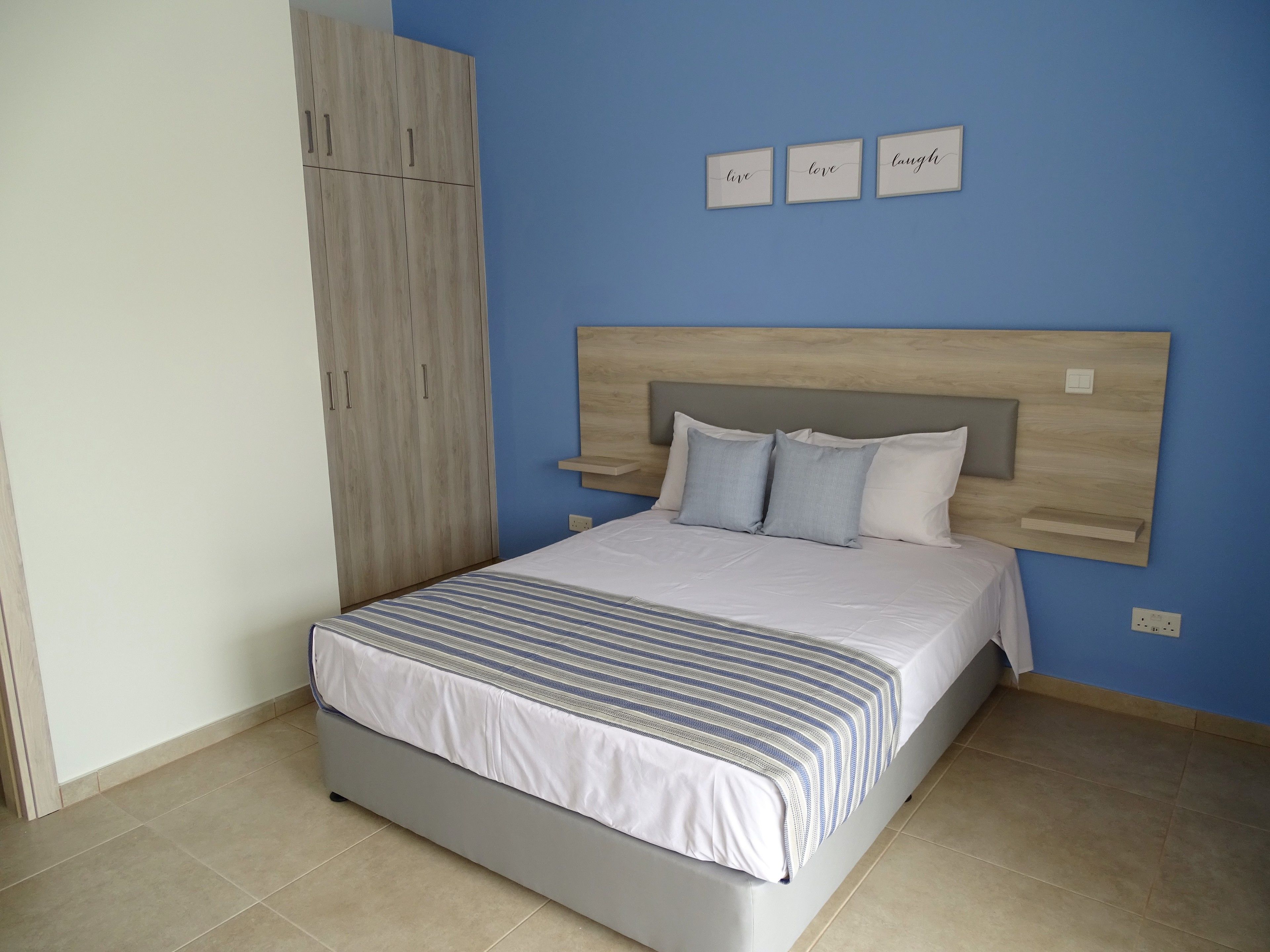 A bedroom with a bed, a wardrobe, and a wall with three framed signs.