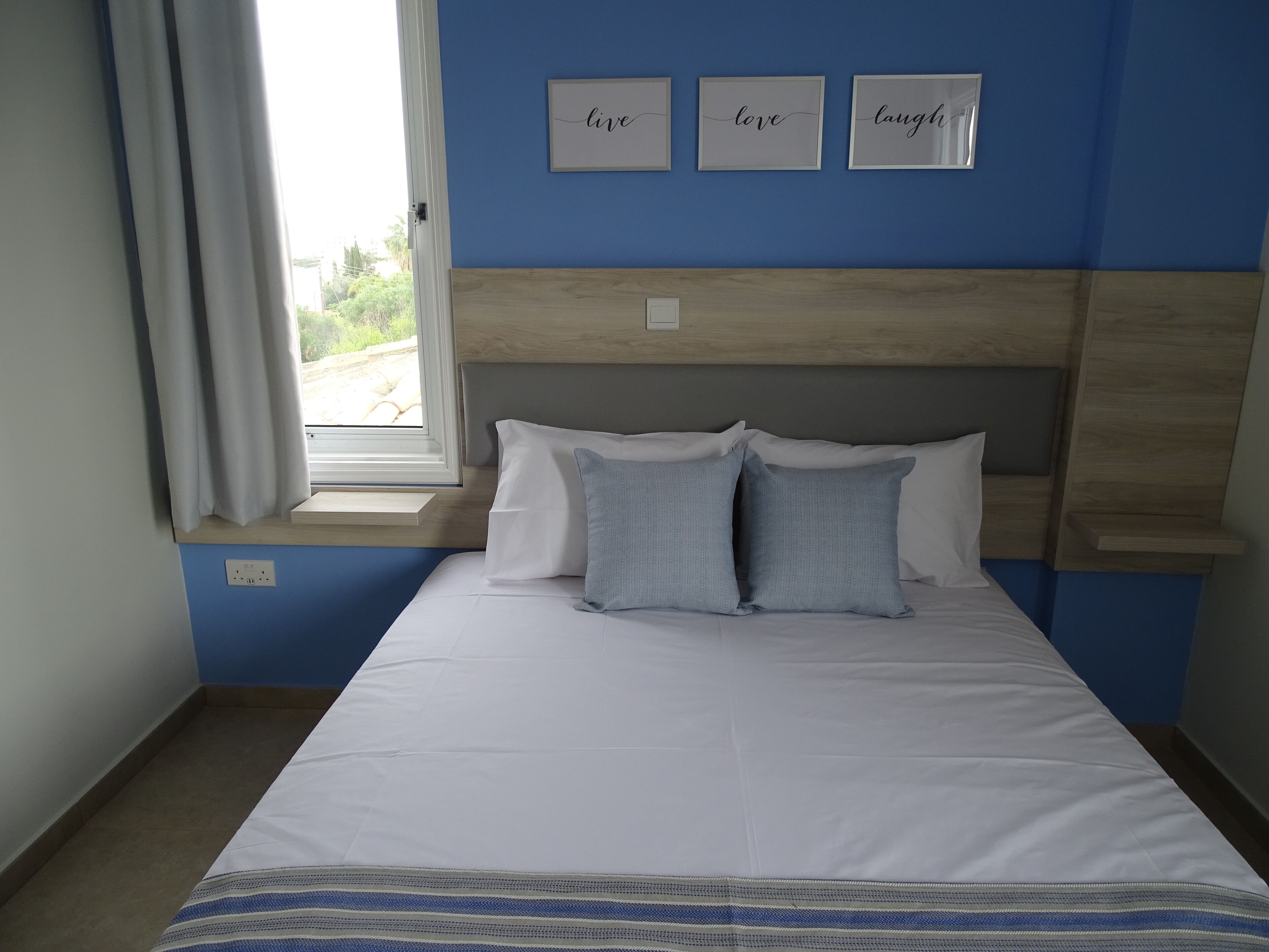 A bedroom with a bed, a window with curtains, and three framed inspirational words on the wall.