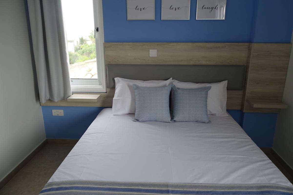 A bedroom with a bed, a window with curtains, and three framed inspirational words on the wall.