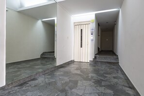 A corridor with a tiled floor, a door with a vertical handle, and a staircase leading to an upper level.