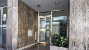 Ein moderner Gebäudeeingang mit Betonfassade, Glasüren und einem Metallgitter.