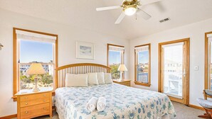 Ein Schlafzimmer mit einem Bett, zwei Nachttischen, einem Deckenventilator und großen Fenstern mit Jalousien.