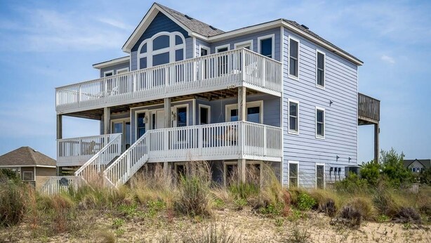 Ein zweistöckiges Strandhaus mit Balkon, Treppe und einer Holzterrasse.