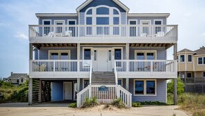 Ein Strandhaus mit zwei Etagen, jeweils mit einem Balkon, einem Hauseingang und einer sichtbaren Garage.