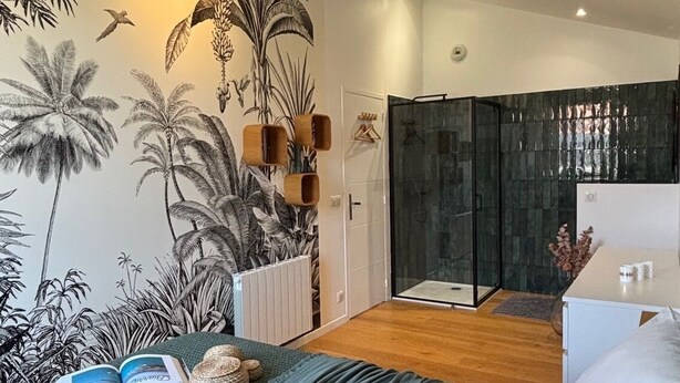 Une chambre moderne avec un grand lit, un espace douche et une fresque murale sur le thème des tropiques.