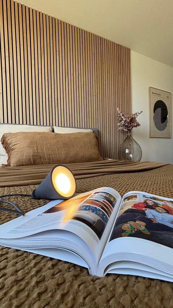A neatly made bed with a wooden headboard, a bedside lamp, a vase with dried flowers, and a Bauhaus poster on the wall. - Villa in the Biarritz Hills: Heated pool, garden, terrace, parking (Biarritz)