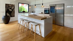 Une cuisine moderne dotée d’un îlot central, de tabourets de bar, de luminaires suspendus et d’appareils électroménagers en acier inoxydable.