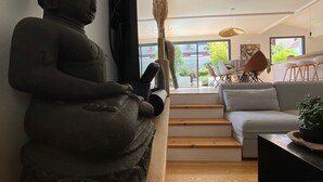 Un salon moderne avec une statue de Bouddha, un plancher en bois, un canapé, une table à manger avec des chaises et un escalier menant à un niveau supérieur.