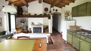 A rustic kitchen with a fireplace, wooden beams, and green cabinets.