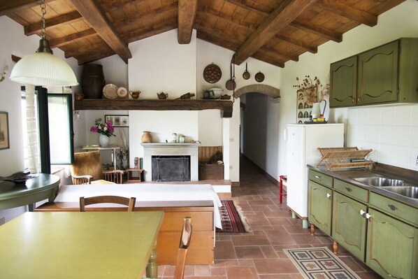 Una cocina rústica con chimenea, vigas de madera y armarios verdes.