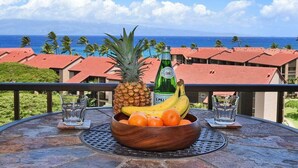 Tropische Umgebung mit gedecktem Tisch, einer Obstschale und einer Flasche, mit Blick auf eine Küstenlandschaft mit roten Dächern und dem Meer.