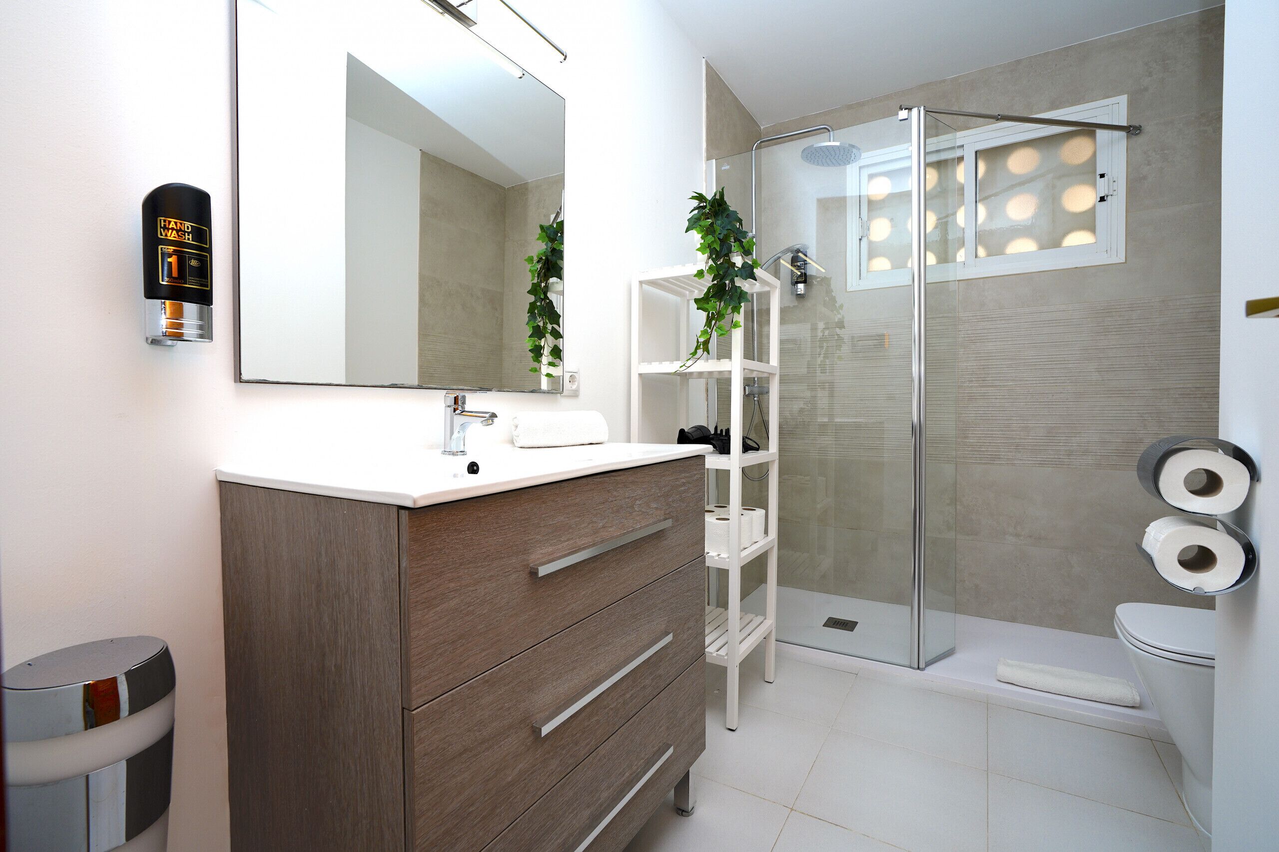 Une salle de bain moderne avec un meuble-lavabo en bois, une cabine de douche en verre et des toilettes avec du papier toilette.