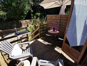 Una terraza de madera con mobiliario exterior, incluyendo sillas, una mesa y una parrilla.