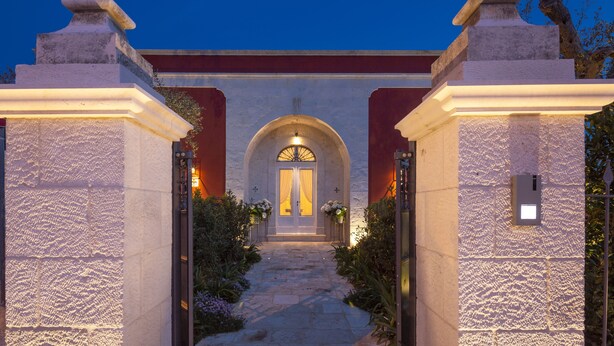 A stone entrance with a central archway leading to a door, flanked by two columns and a pathway with plants. - Dimora Graziana (Locorotondo)