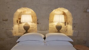 A bed with white linens, two wall-mounted lamps, and a brick wall. - Dimora Graziana (Locorotondo)