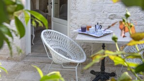 A white wicker chair and a table with a tray of breakfast items in a stone-walled outdoor area. - Dimora Graziana (Locorotondo)