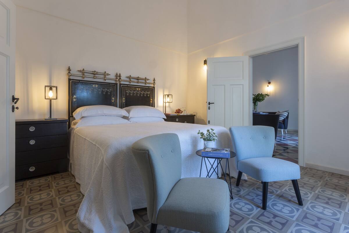 A bedroom with a large bed, two bedside tables, a chair, and a small table with a plant.