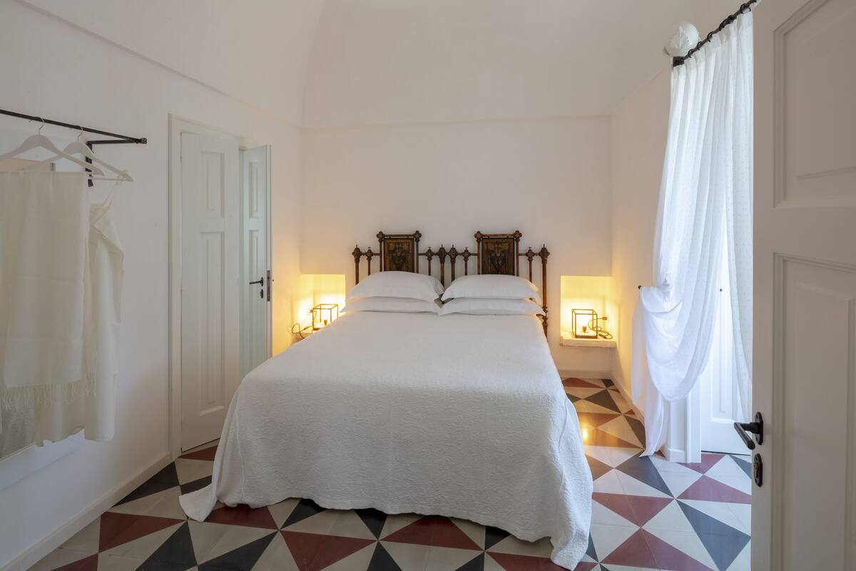A bedroom with a bed, a door, a coat rack, and a patterned floor.