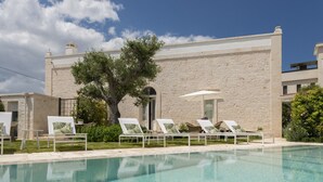 A pool area with lounge chairs and a stone building in the background. - Dimora Graziana (Locorotondo)